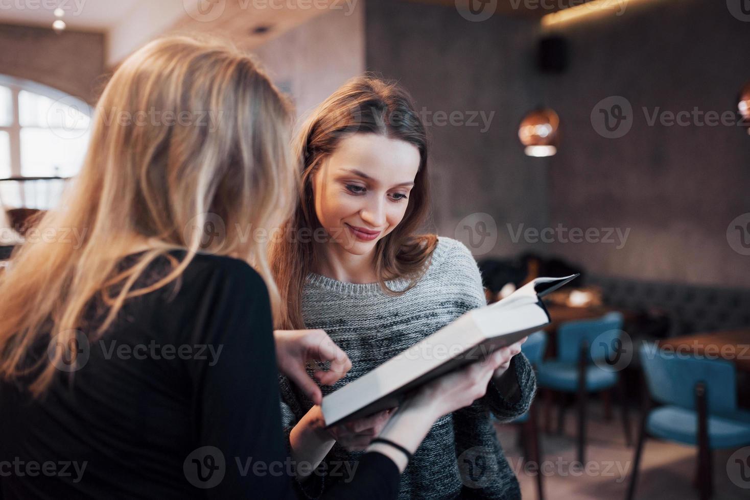 två unga kvinnor sitter på kaféet och dricker kaffe och njuter av bra böcker. studenter på fikapaus. utbildning, livsstilskoncept foto