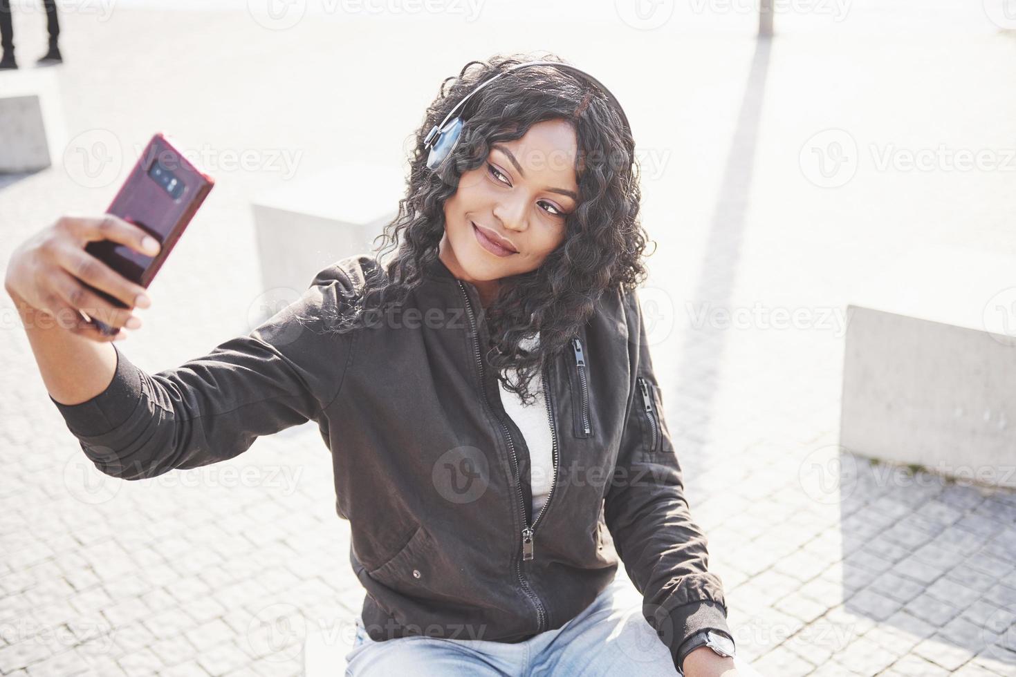 porträtt av en vacker ung söt afroamerikansk flicka som sitter på stranden eller sjön och lyssnar på musik i sina hörlurar foto