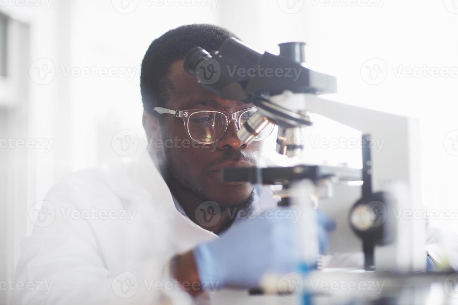forskaren arbetar med ett mikroskop i ett laboratorium som utför experiment och formler. foto