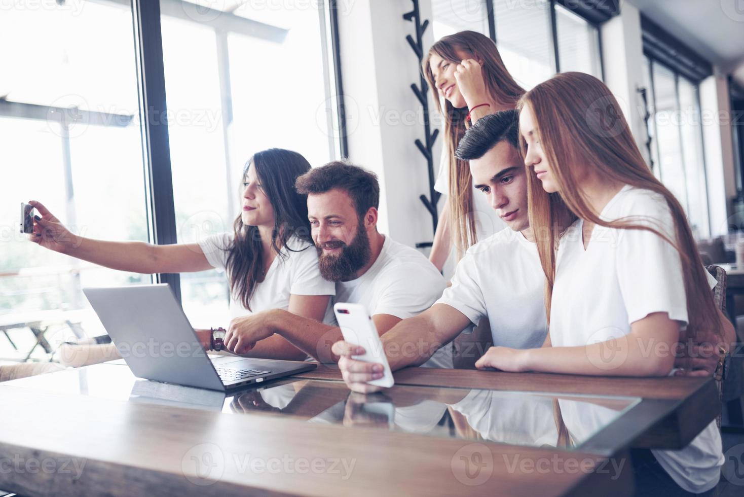 en grupp människor gör ett selfiefoto på ett kafé. vänner och studenter samlades kring den bärbara datorn och förbereder ett gemensamt projekt foto