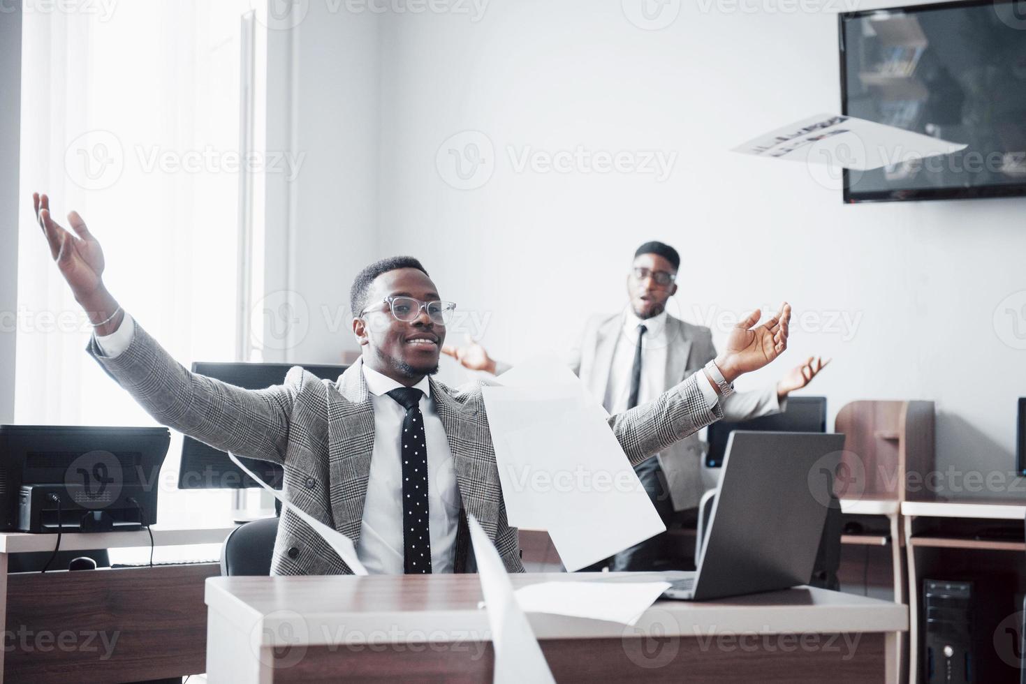 två stiliga glada afroamerikanska affärsman firande framgångsrika med att kasta papper på arbetsplatsen foto