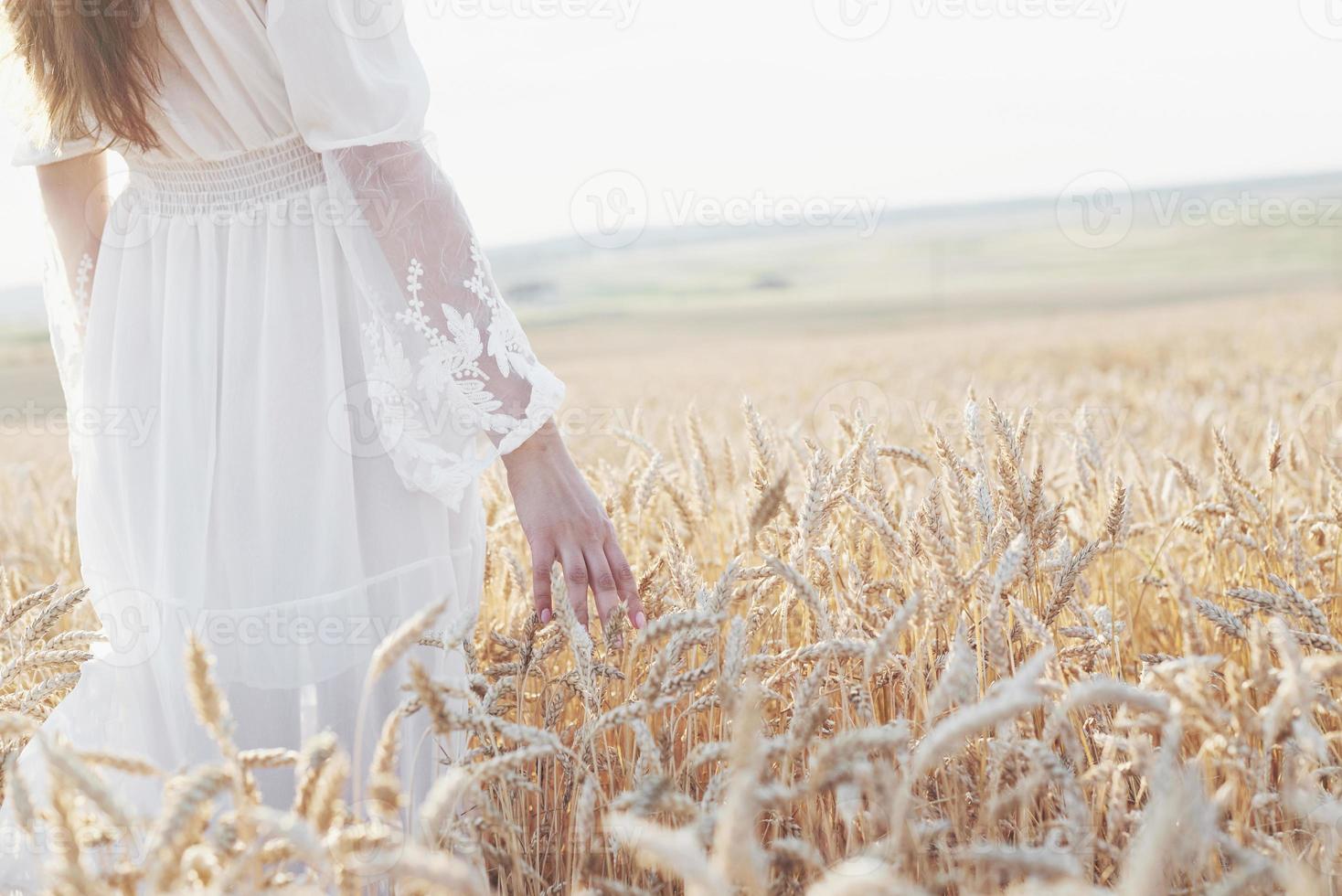 vacker flicka i vit klänning som körs på höstfältet av vete vid solnedgången foto