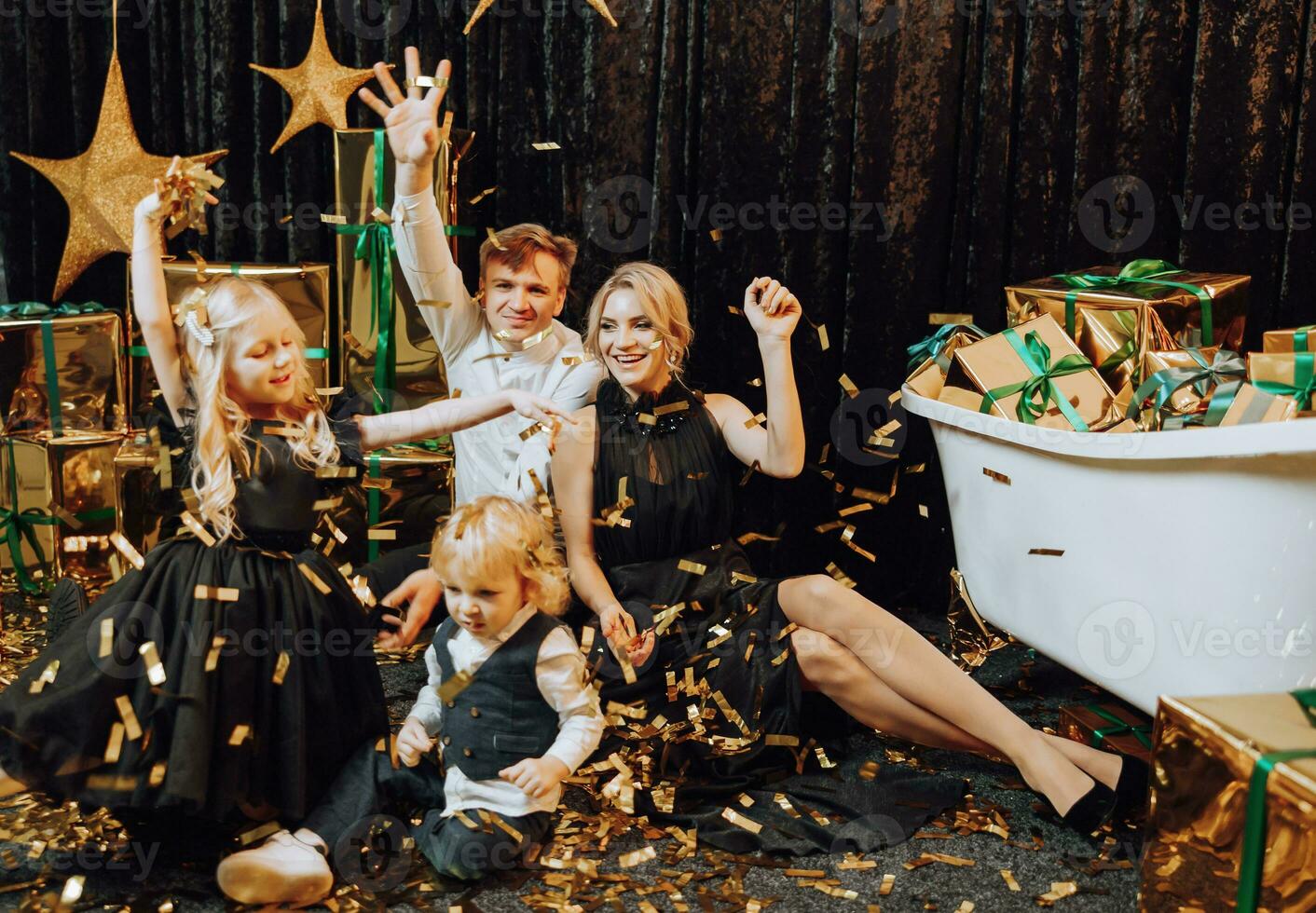 glad jul och Lycklig högtider. glad och Lycklig familj med jul gåvor i gyllene förpackning och mörk bakgrund spelar med konfetti. kärleksfull familj med gåvor i de rum. foto