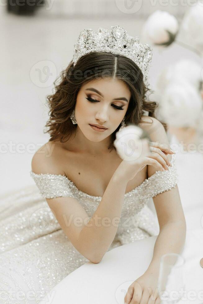 studio Foto av en prinsessa i en bröllop klänning med en lyxig frisyr och smink, de brud är Sammanträde på de tabell