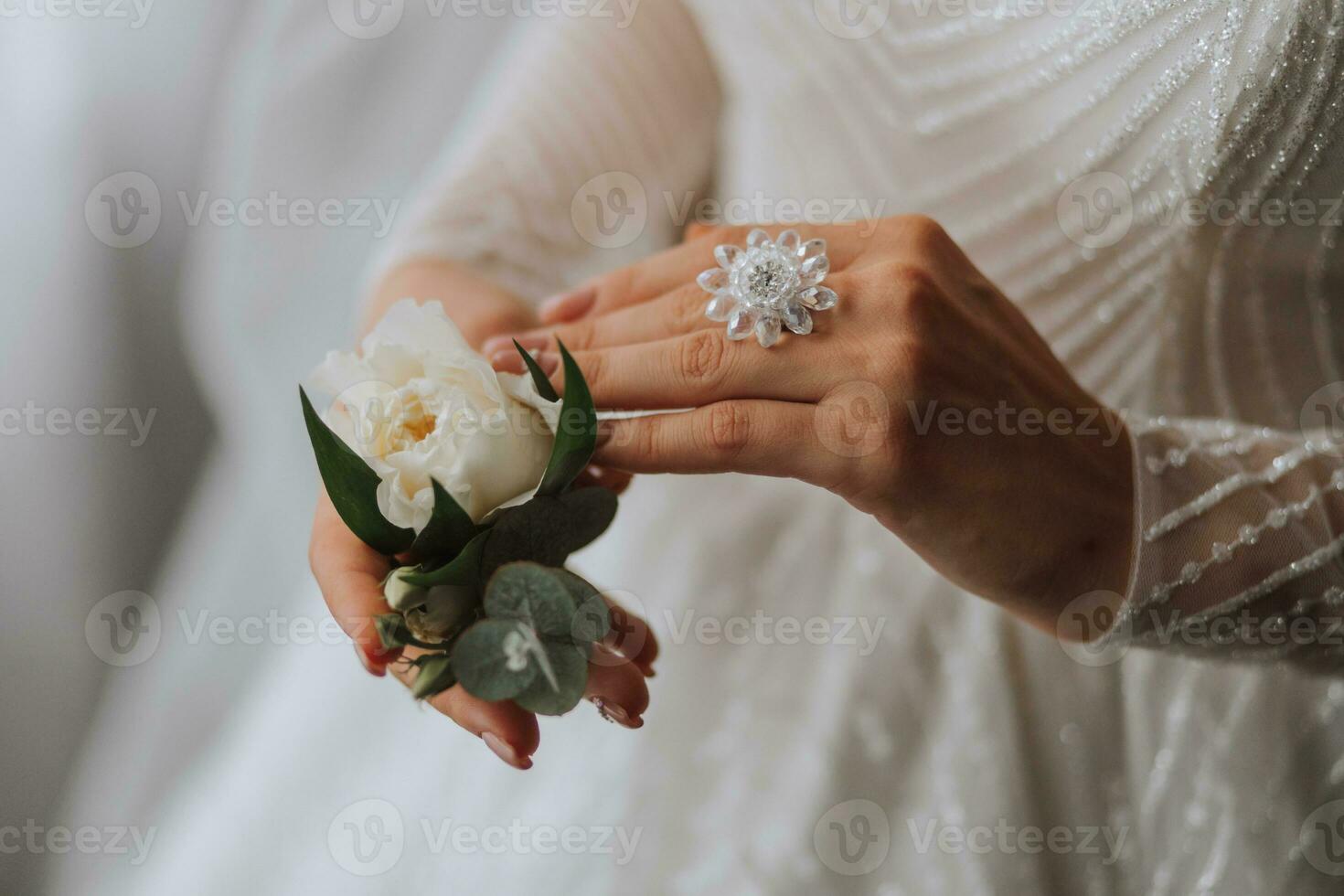 detaljer bröllop Tillbehör. de brud är innehav en vit reste sig, en skön bröllop ringa med en kristall på henne hand. beskurna Foto. skön händer foto