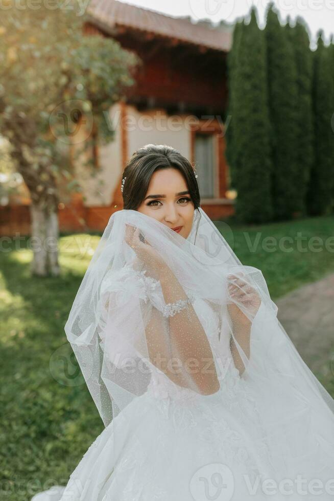 skön brud i en modern bröllop klänning på en naturlig bakgrund i de parkera. en fantastisk ung brud är otroligt Lycklig. Lycklig flicka på henne bröllop dag foto