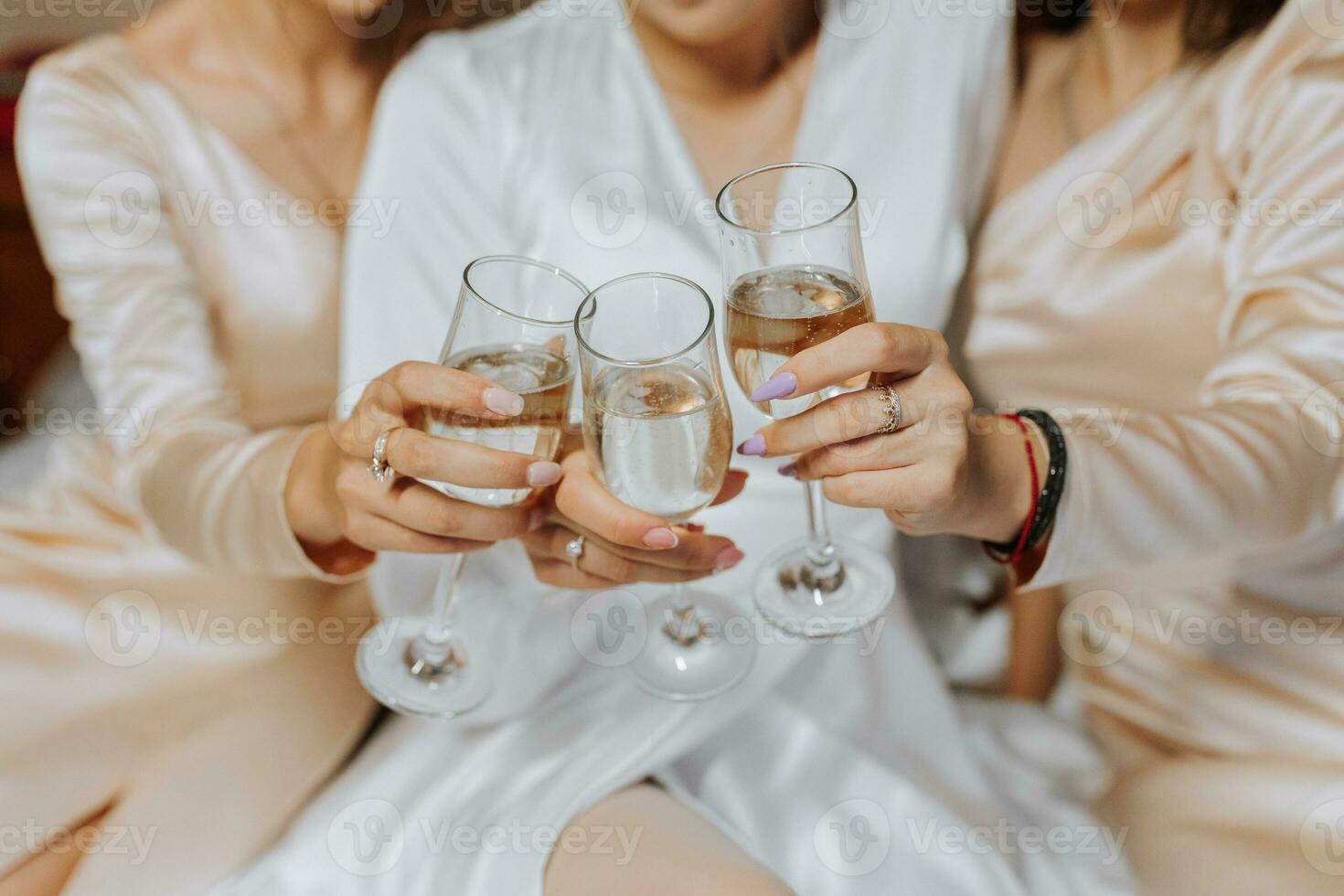 leende brud och henne vänner är Sammanträde på de säng i de sovrum och dricka champagne foto