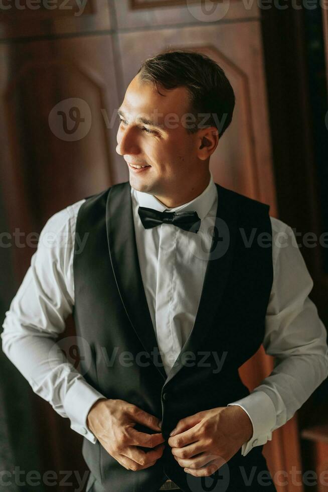 förberedelse för de morgon- av de brud och brudgum. porträtt Foto av ett elegant man få klädd för en bröllop firande. de brudgum, klädd i en vit skjorta och rosett slips