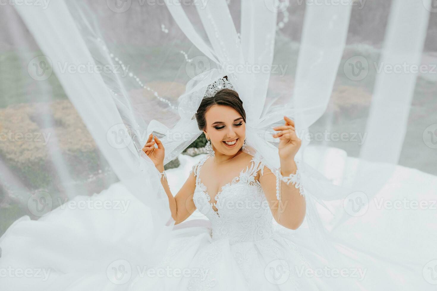 ett elegant brunett brud poser under en slöja i en vit klänning. porträtt av de brud, bröllop smink och frisyr, bröllop mode. skön brud i en slöja foto