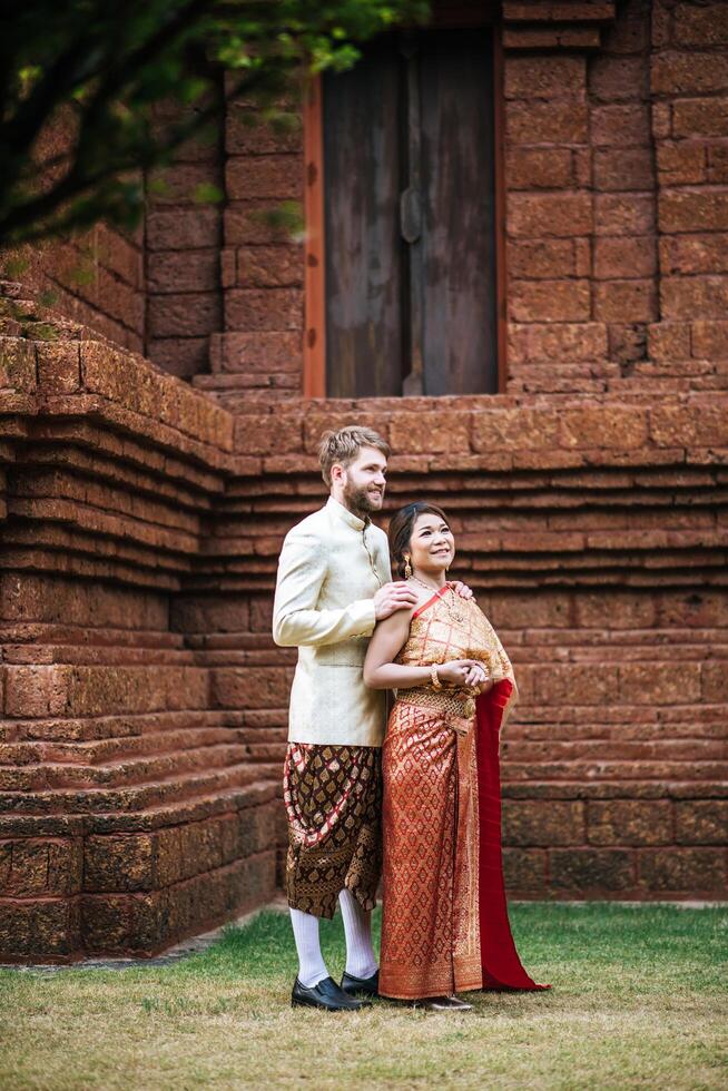 asiatisk brud och kaukasisk brudgum har romantisk tid med thailändsk klänning foto