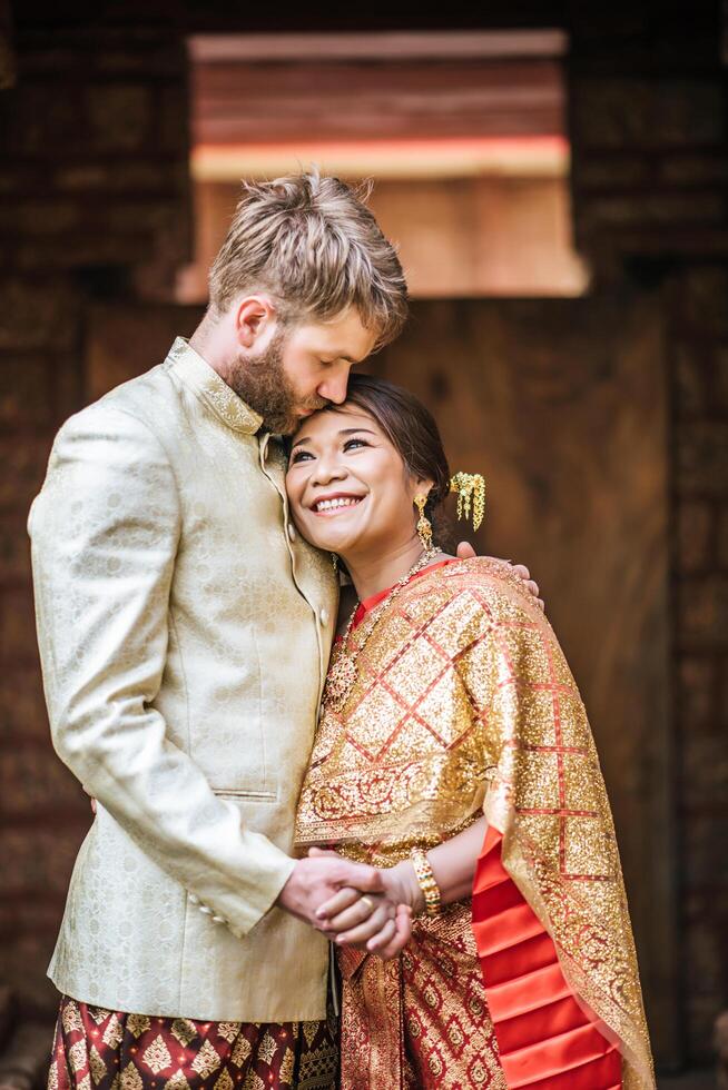 asiatisk brud och kaukasisk brudgum har romantisk tid med thailändsk klänning foto