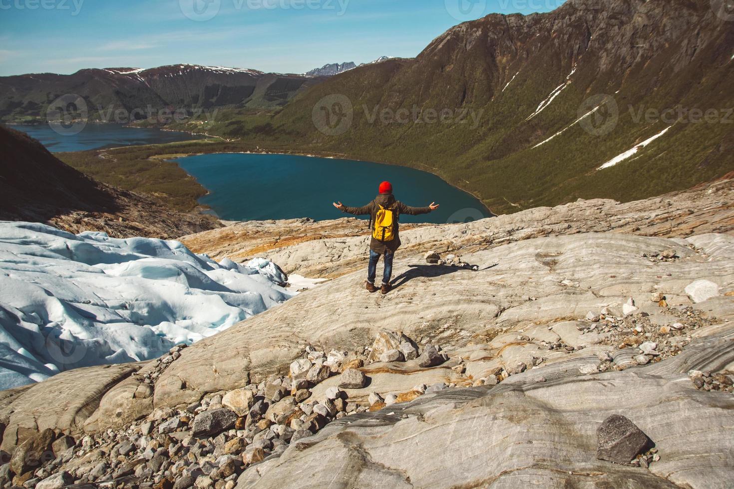 man med en ryggsäck som står på en sten på bakgrund av berg och sjö foto