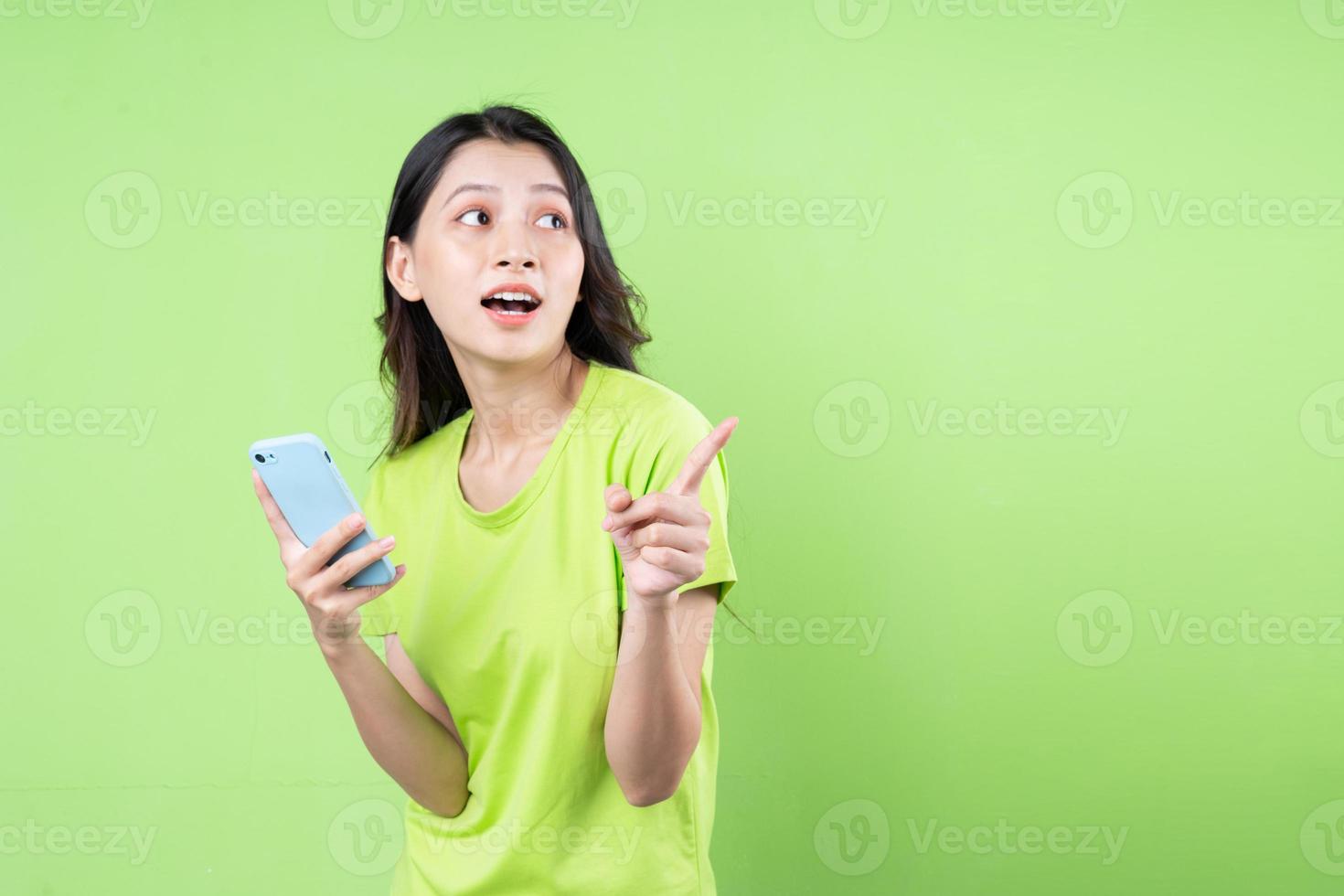 bild av ung asiatisk kvinna som håller smartphone på grön bakgrund foto