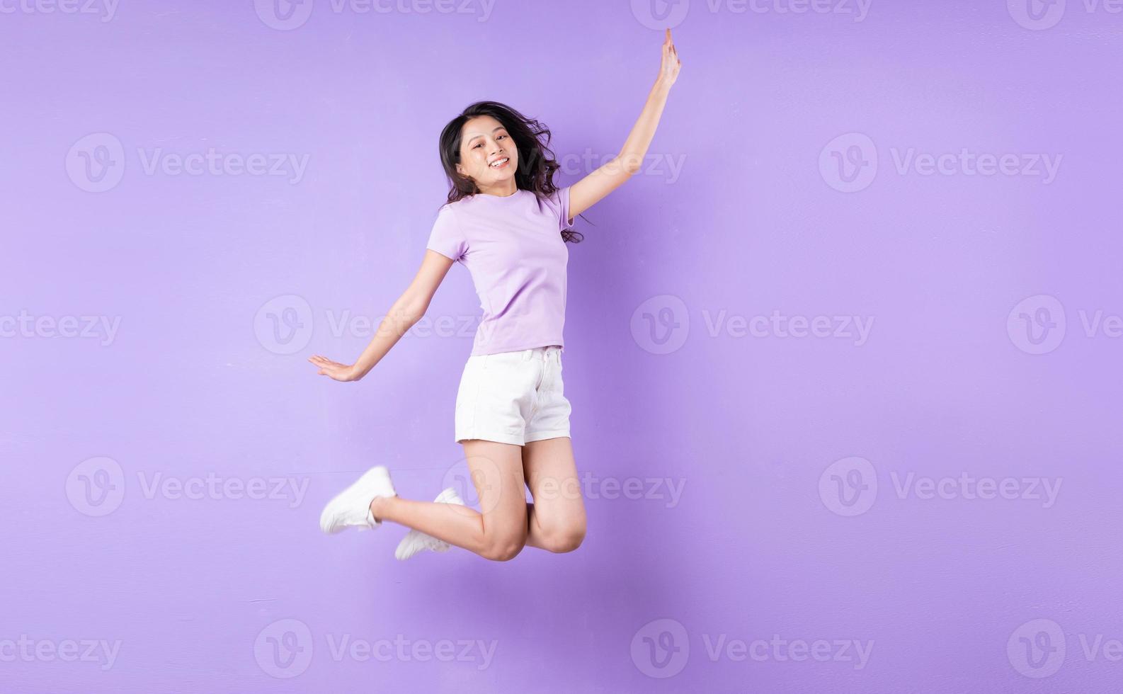 ung asiatisk tjej som hoppar upp på lila bakgrund foto