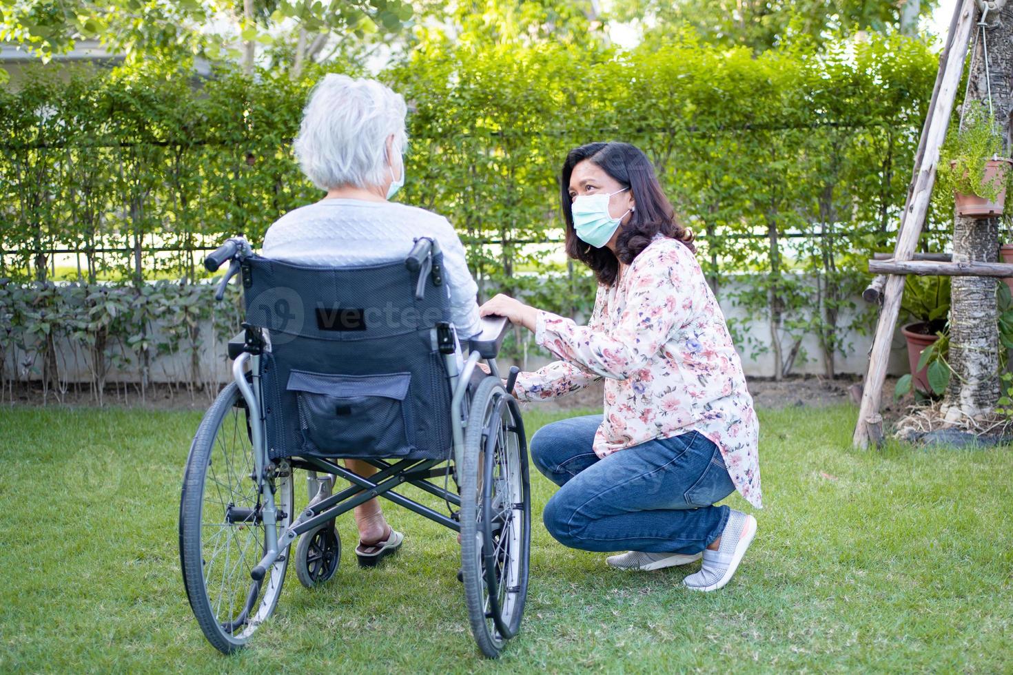 hjälp asiatisk senior eller äldre gammal damkvinna på rullstol och bär ansiktsmask för att skydda säkerhetsinfektion covid-19 coronavirus i parken. foto