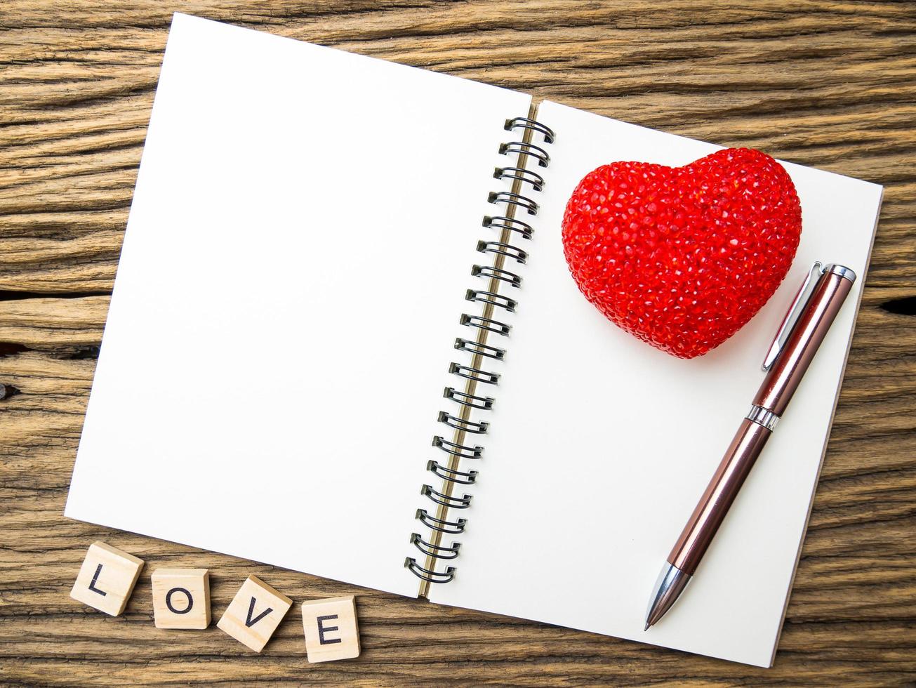 ovanifrån av anteckningsbok och penna med rött hjärta på trä svart bakgrund, kärleksord i träkub, alla hjärtans dag foto