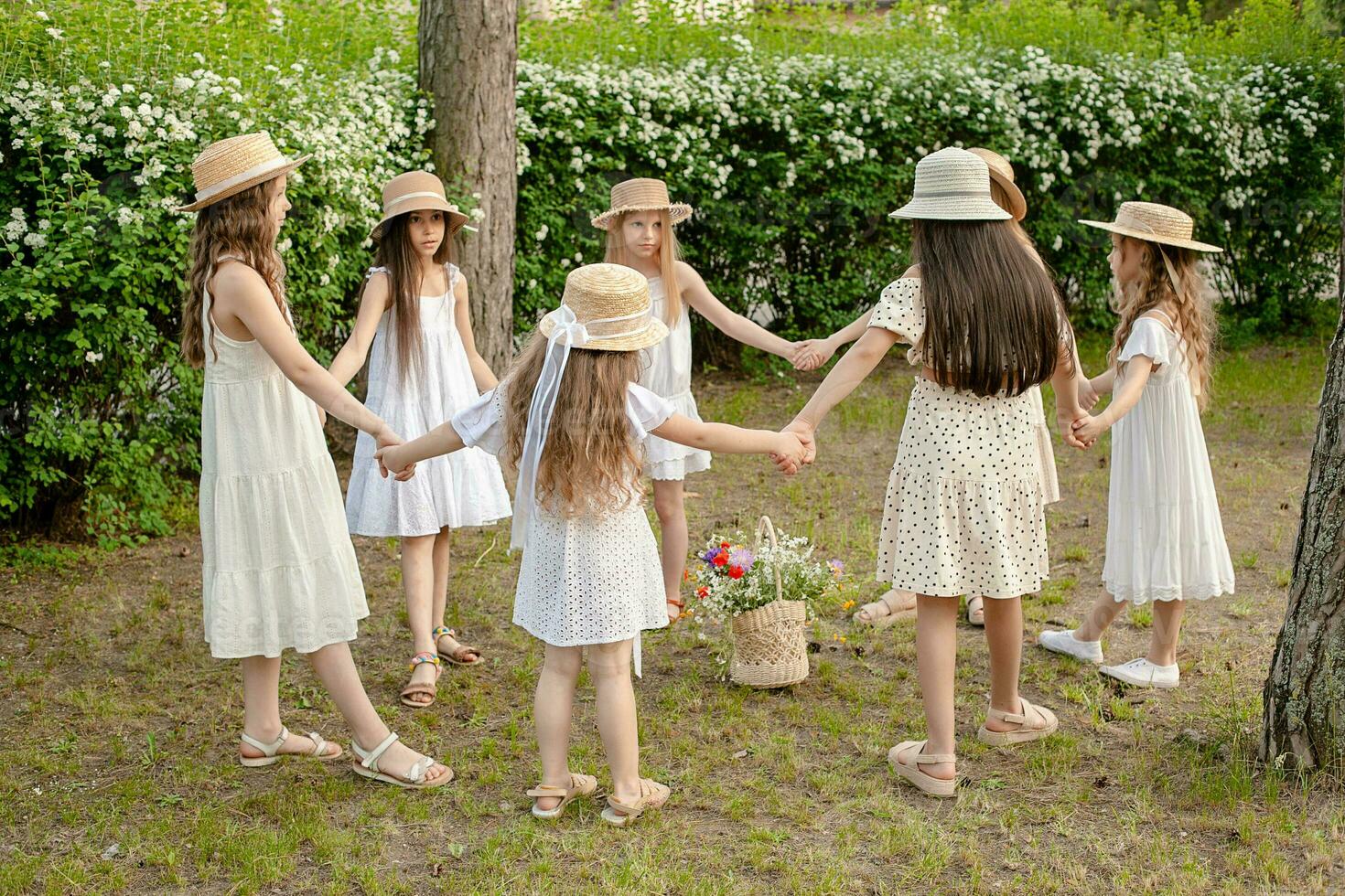 grupp av preteen flickor i ljus klänningar dans i cirkel i grön sommar parkera foto