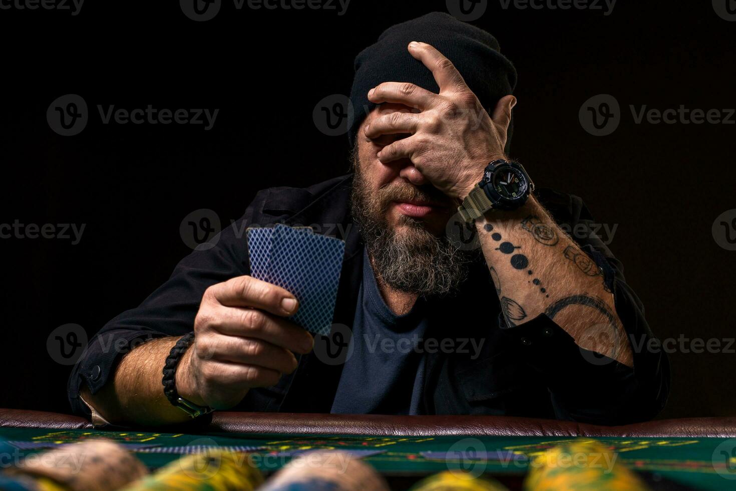 allvarlig skäggig man Sammanträde på poker tabell och innehav kort isolerat på svart foto