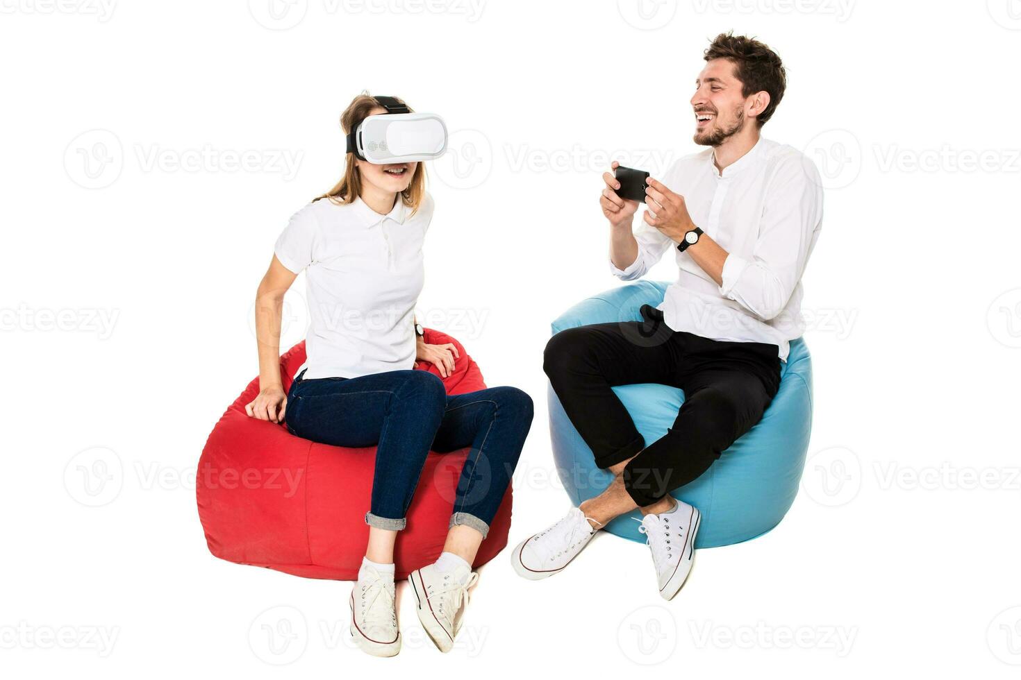 leende vänner upplever virtuell verklighet glasögon sittande på Bönpåsar isolerat på vit bakgrund. foto