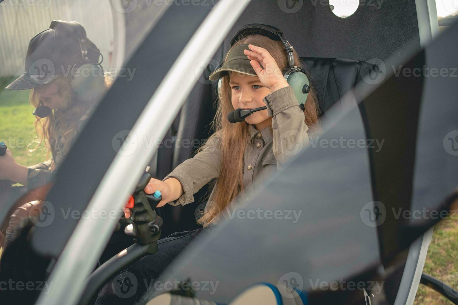 två fokuserade preteen flickor i flygare headsets Sammanträde i helikopter cockpit foto