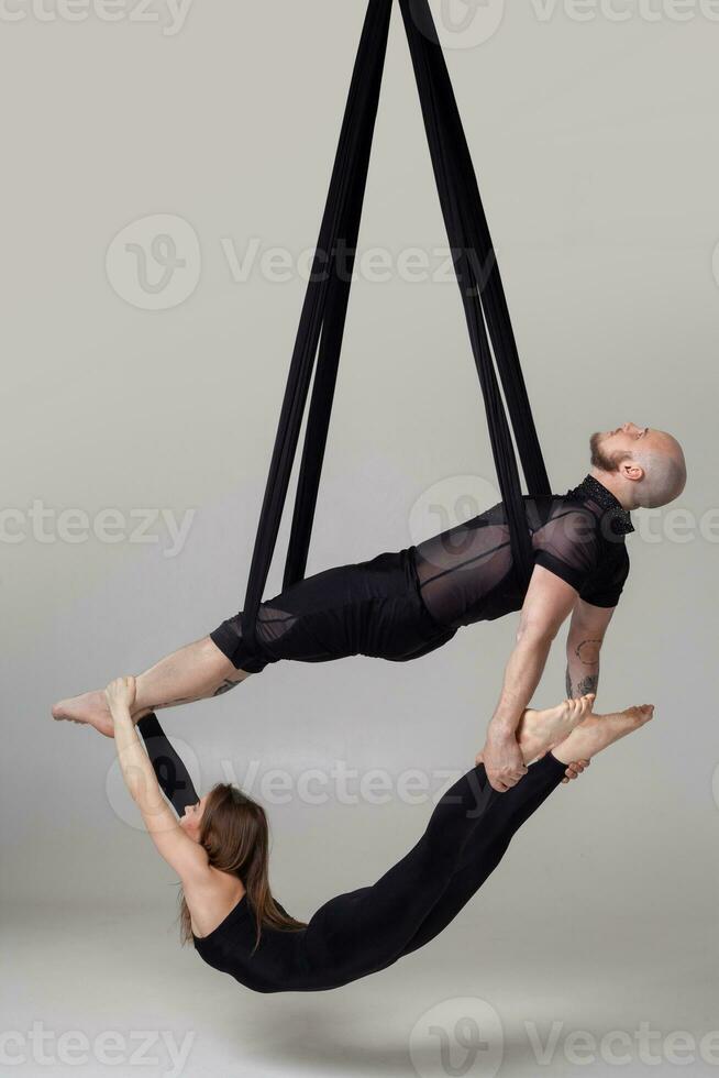 skön flicka och ett atletisk man i en svart sport kostymer är utför ett akrobatisk element i en studio. foto