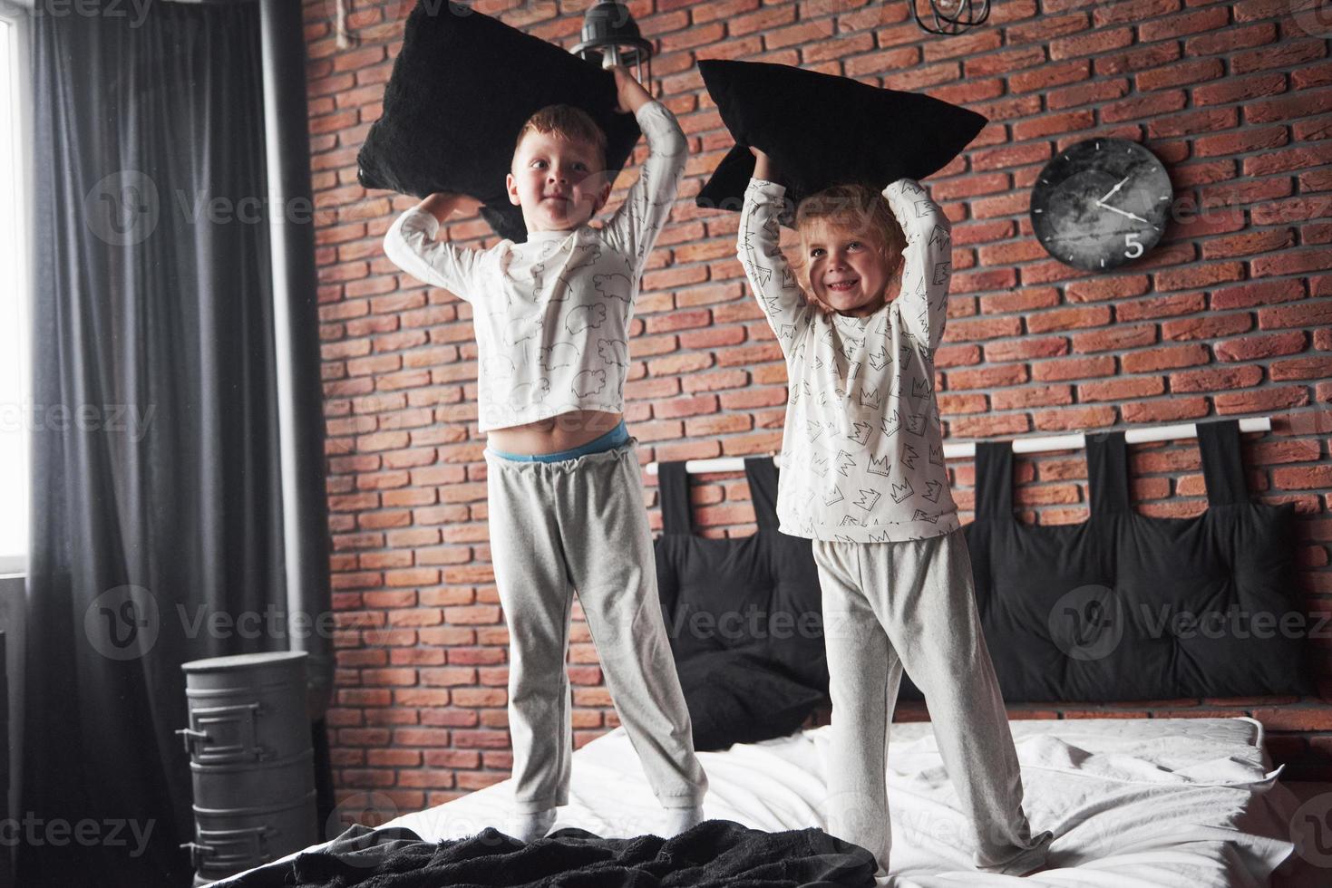 stygga barn liten pojke och flicka iscensatte en kudde slagsmål på sängen i sovrummet. de gillar den typen av spel foto