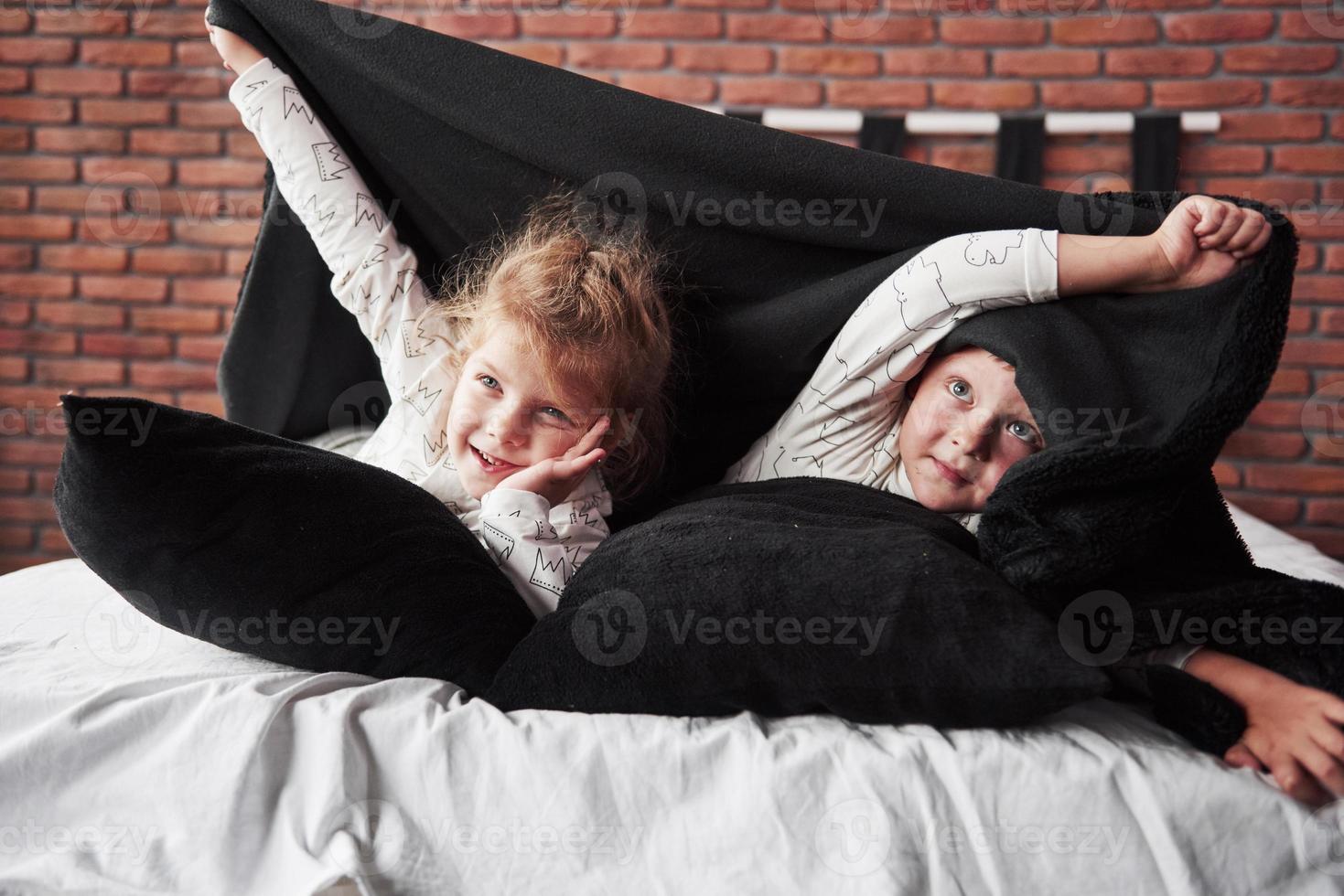 små barn, pojke och flicka som låg och lekte med kuddar på sängtäcket med en filt foto