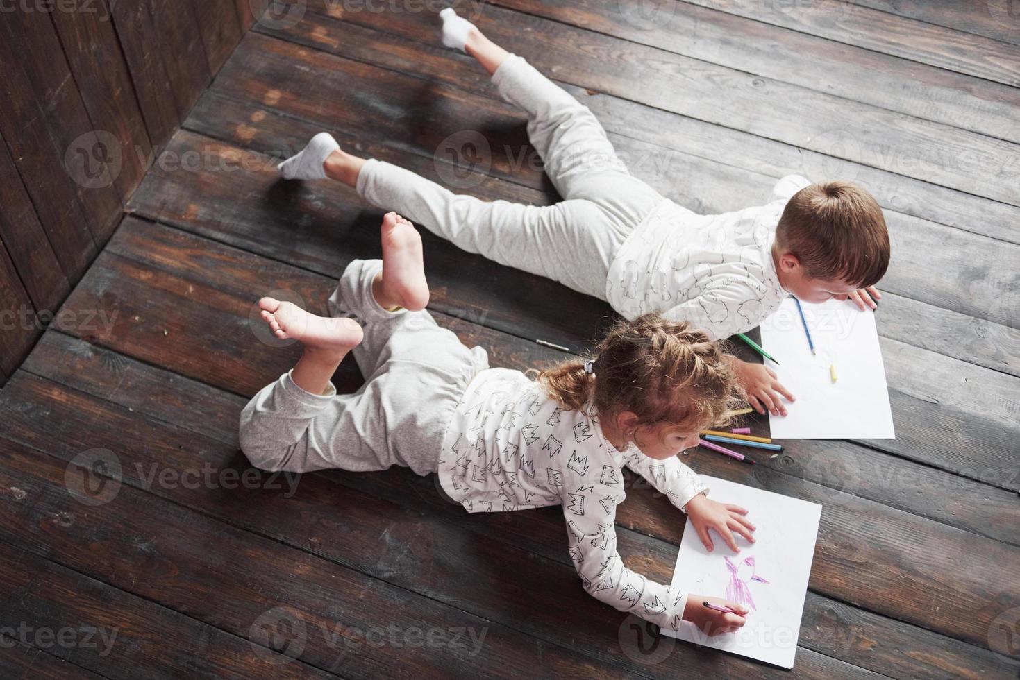 barn ligger på golvet i pyjamas och ritar med pennor. söt barnmålning av pennor foto