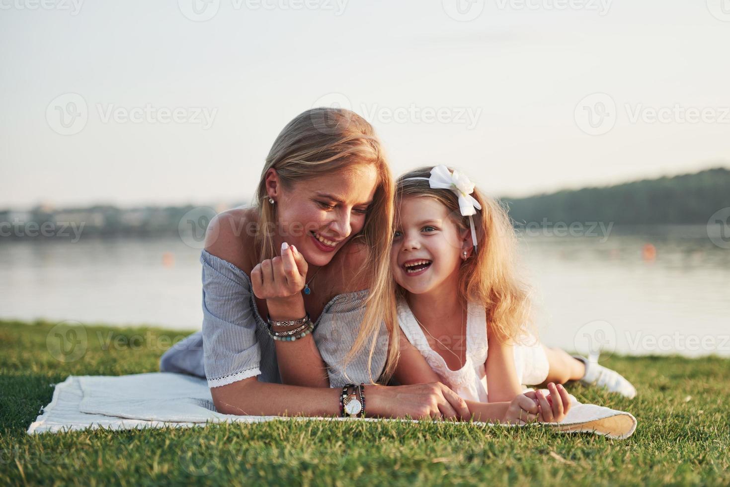 attraktiv glad ung mamma som ligger med sin söta dotter på gräset i parken. foto