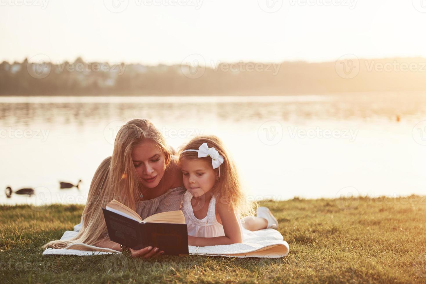 mamma med ett barn läser en bok på gräset foto