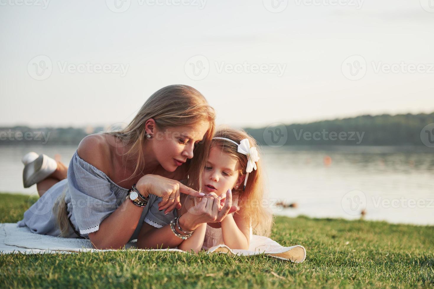 attraktiv glad ung mamma som ligger med sin söta dotter på gräset i parken. foto