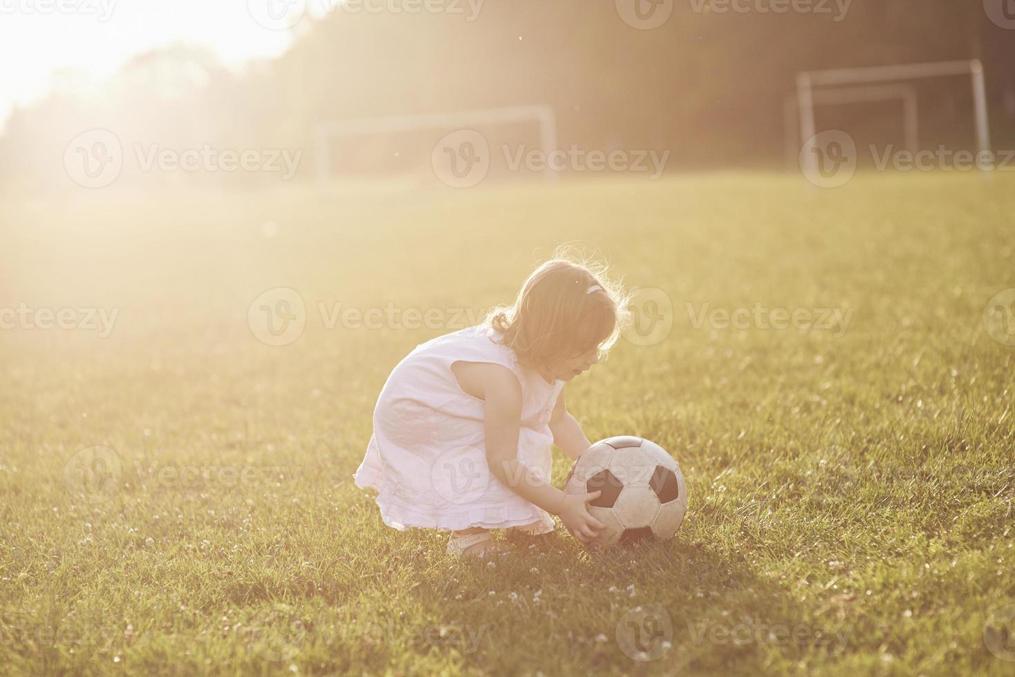 liten flicka spelar boll i fältet vid solnedgången foto