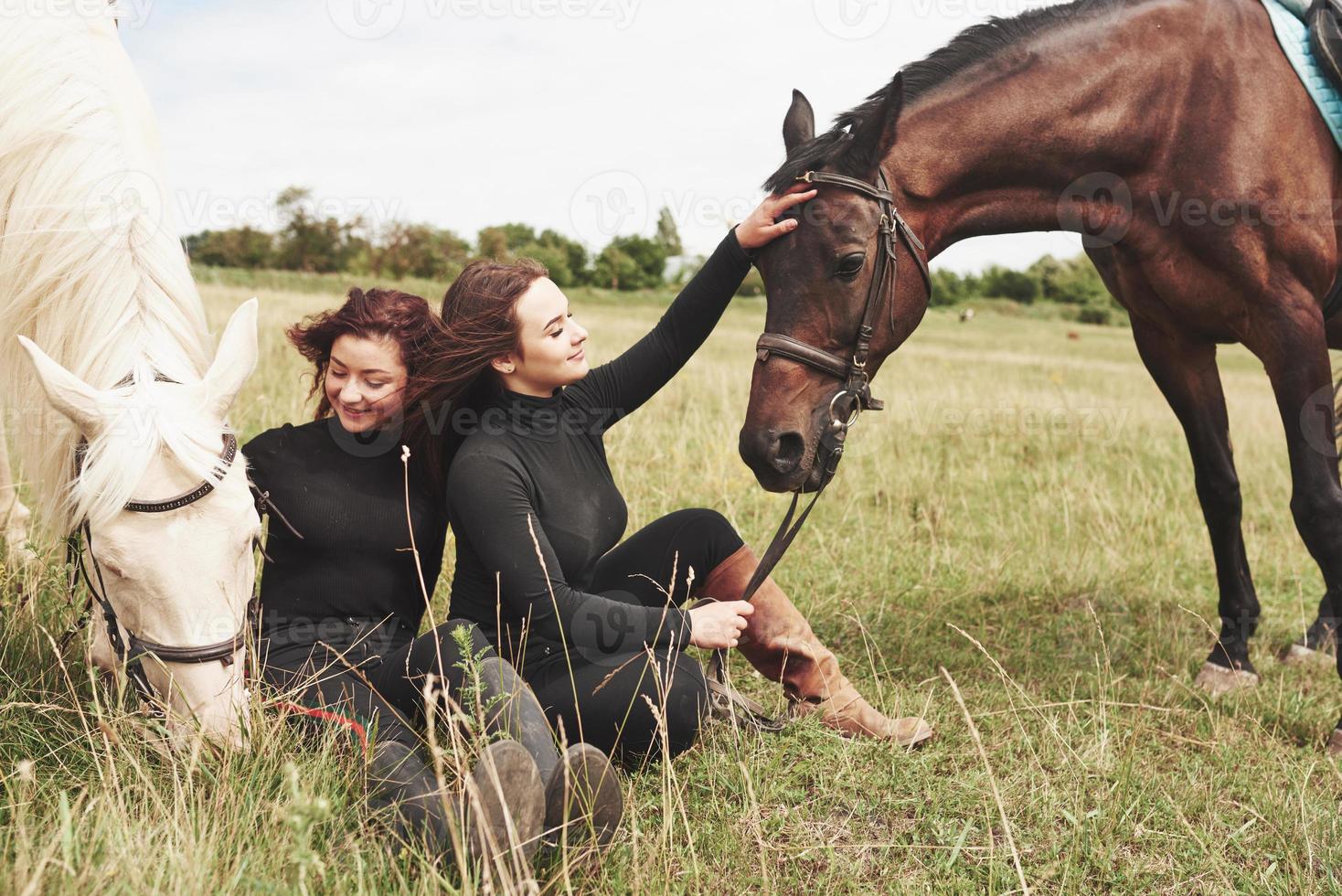 två unga vackra tjejer i redskap för ridning nära sina hästar. de älskar djur foto