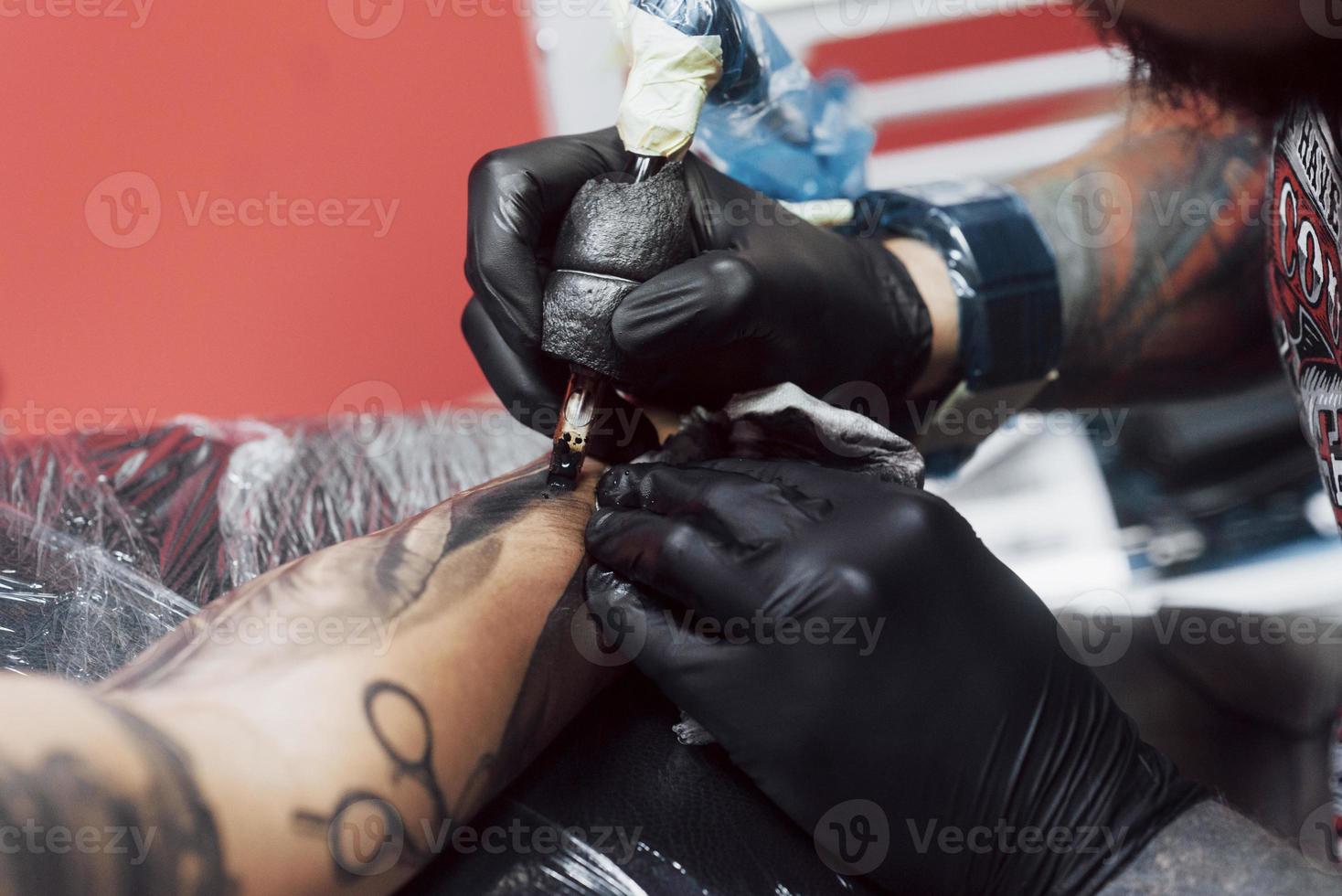 närbild tatuering maskin. mästare i svarta sterila handskar skapar bild till hands med den i salongen foto