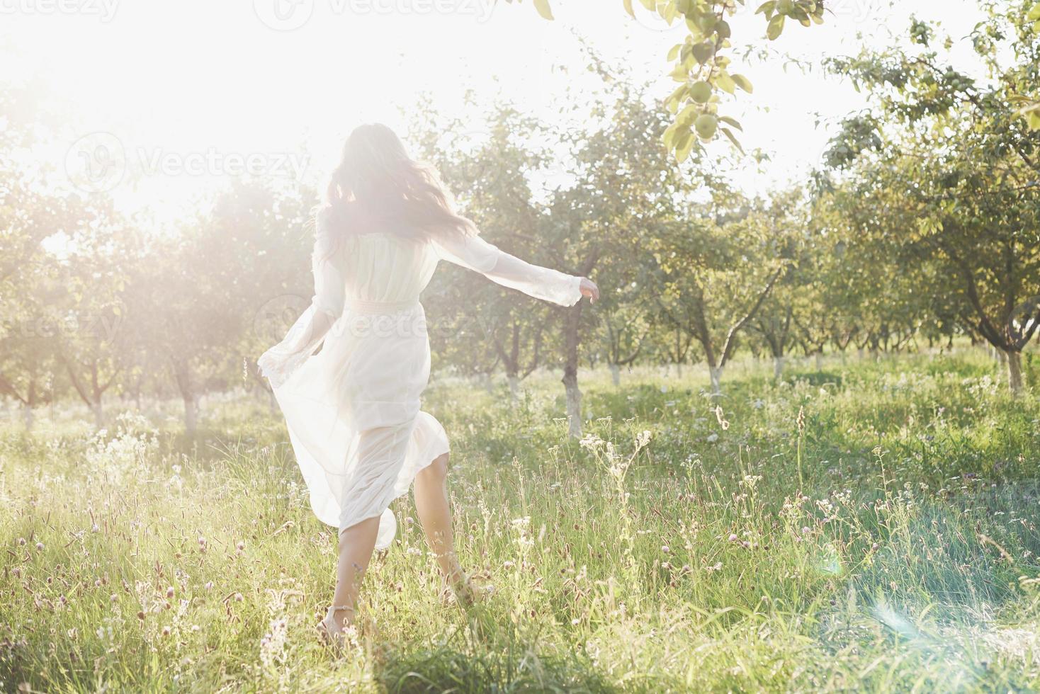 vacker ung kvinna klädd i elegant vit klänning och njuter av vacker solig eftermiddag i en sommar trädgård foto