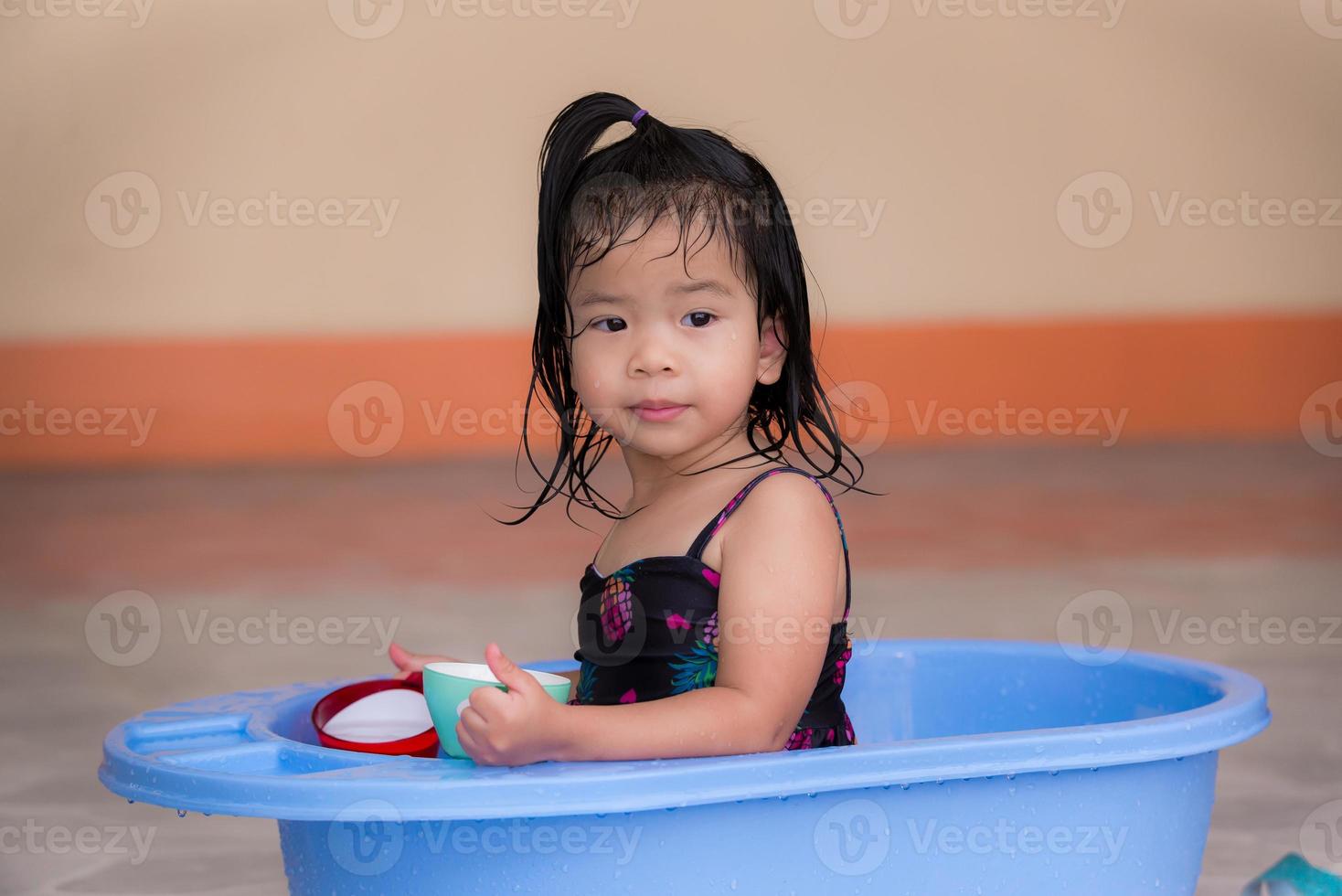 flicka i baddräkt, leker i det blå bassängen framför hennes hus. barn leker plastmuggar, leksaker från omgivningen i det dagliga livet. söt liten unge, 3 år. foto