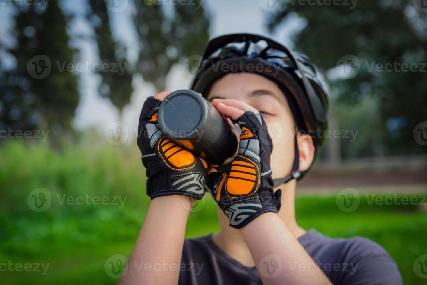 ung pojke med cykelhjälm som dricker från en svart plastflaska foto