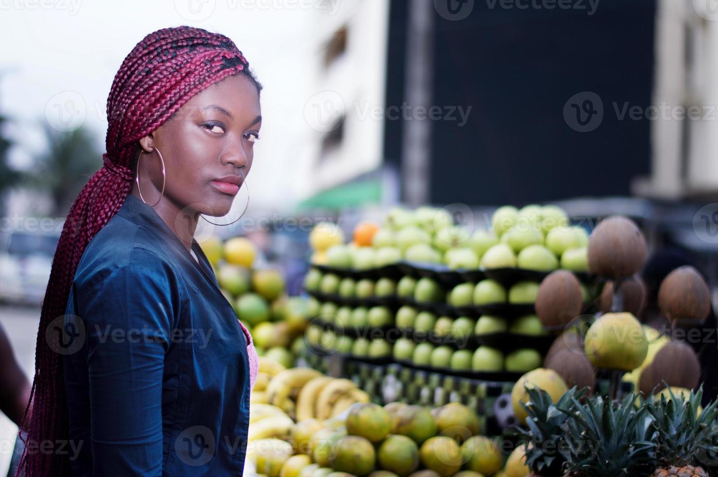 ung kvinna som står framför hyllor med frukt till marknaden. foto