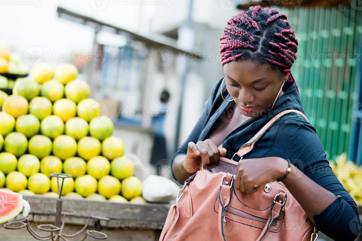 ung kvinna framför en hög med apelsiner, tittar i handväskan. foto