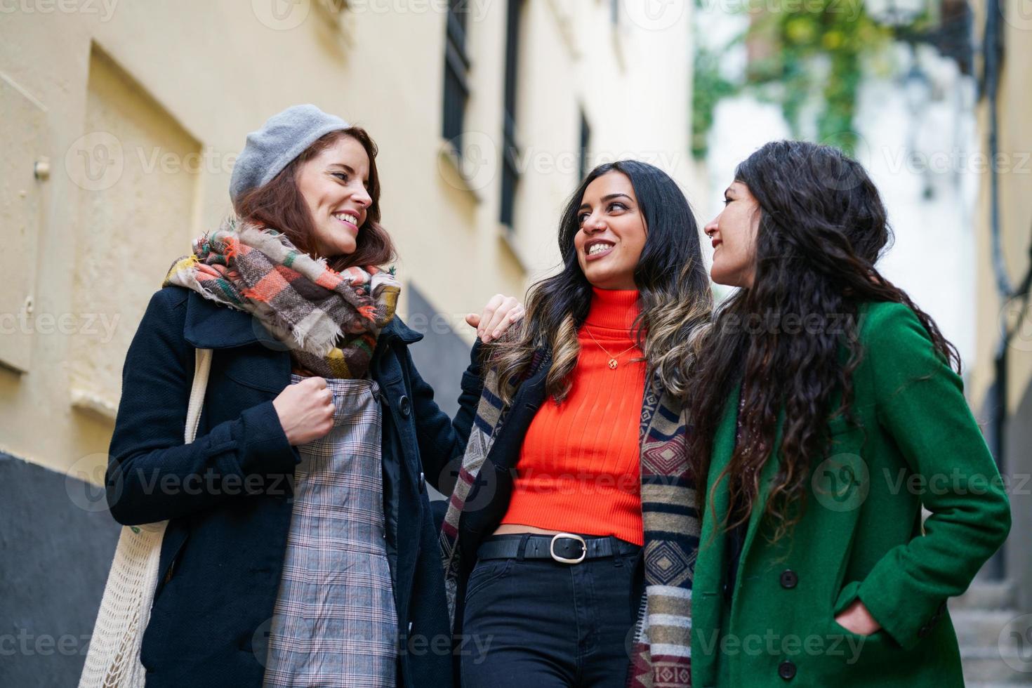 multietnisk grupp av tre glada kvinnor som går tillsammans utomhus foto