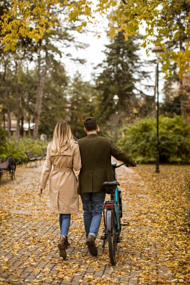 bakifrån på ungt par i höstparken med elektrisk cykel foto