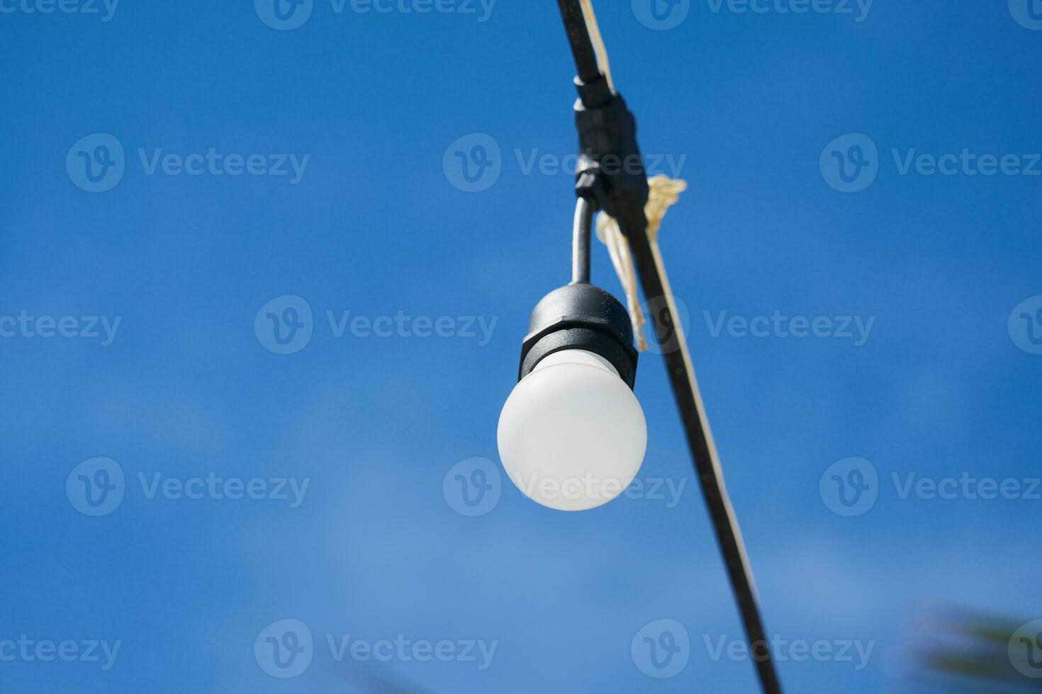 ljus Glödlampa på en tråd med blå himmel på de bakgrund. foto