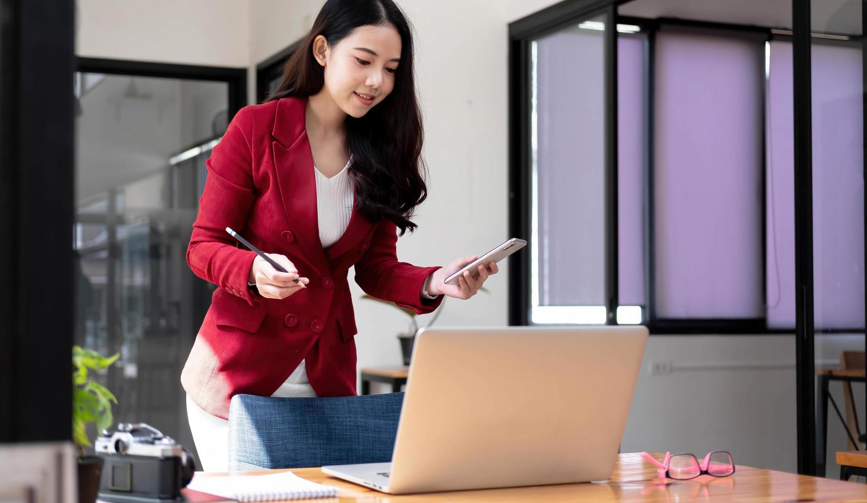 leende asiatisk kvinna som håller mobiltelefon med näven och är upphetsad för framgång på kontoret foto