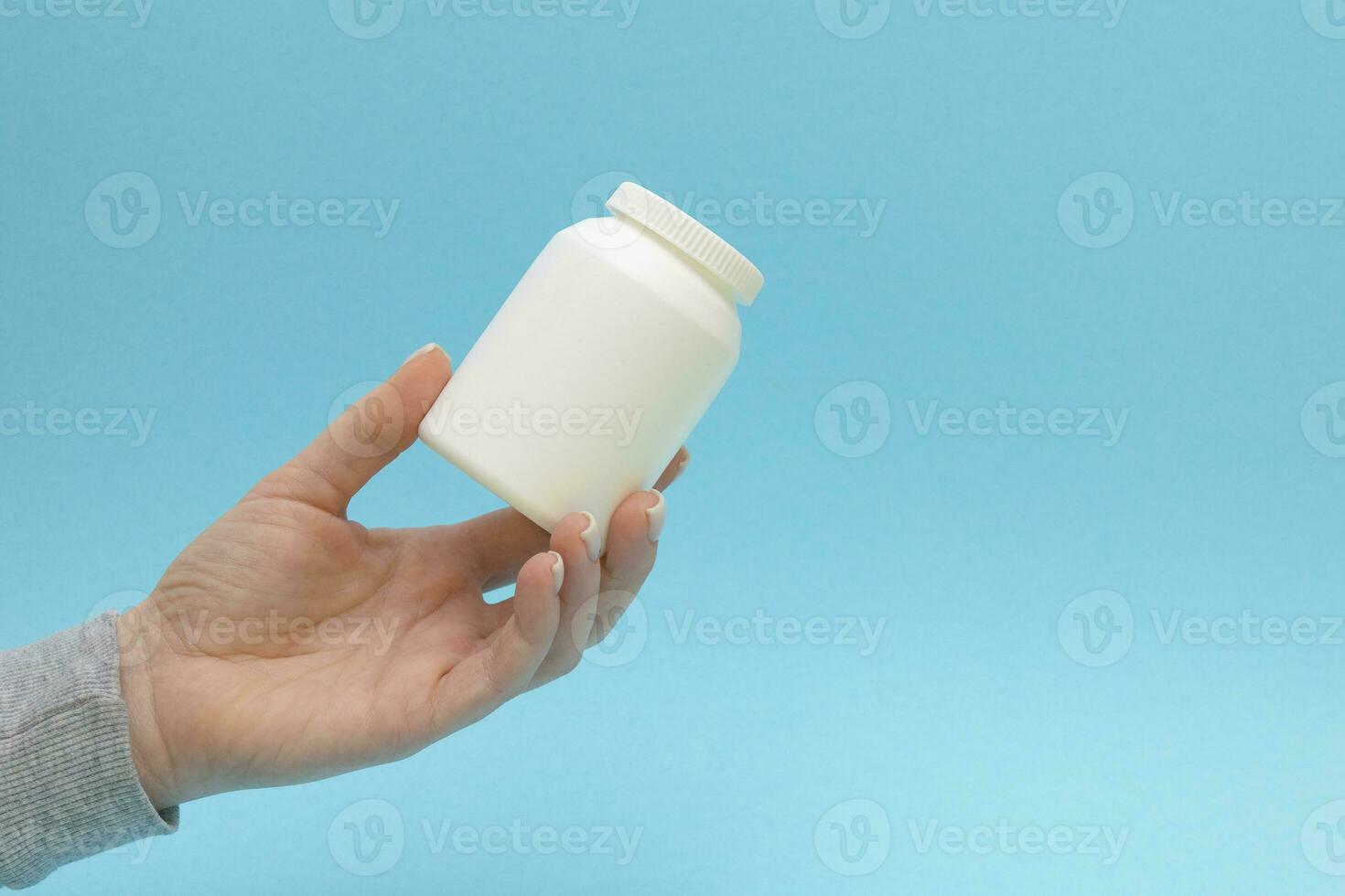 de piller flaska, medicin behållare för vitaminer i kvinna hand på blå bakgrund. foto