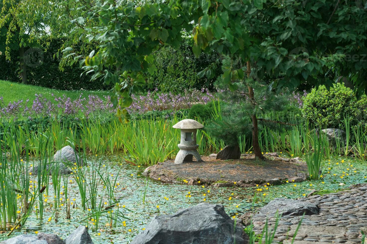 sten lykta på en små ö i de mitten av en damm i en japansk trädgård foto