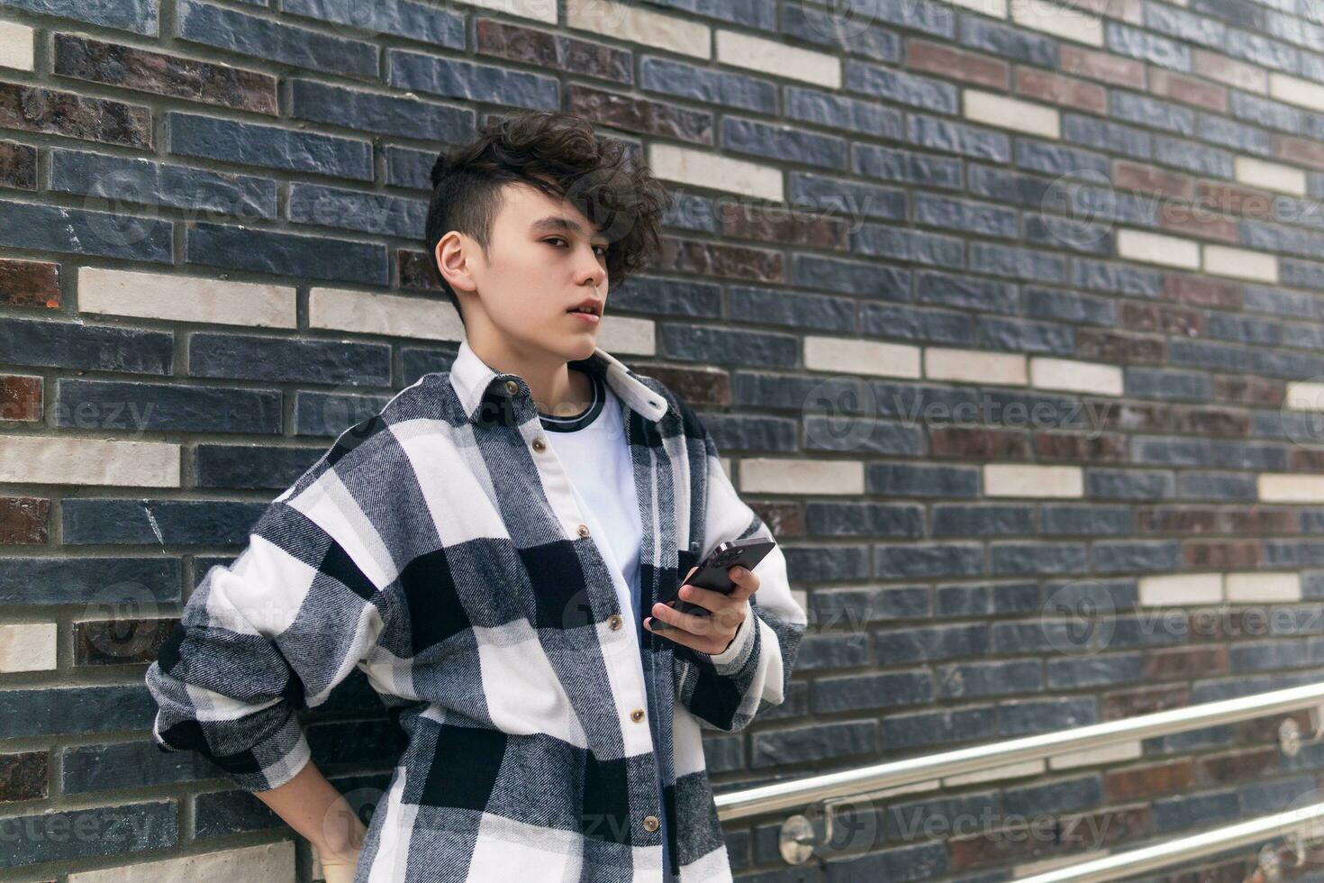 ung man med en telefon mot en tegel vägg foto