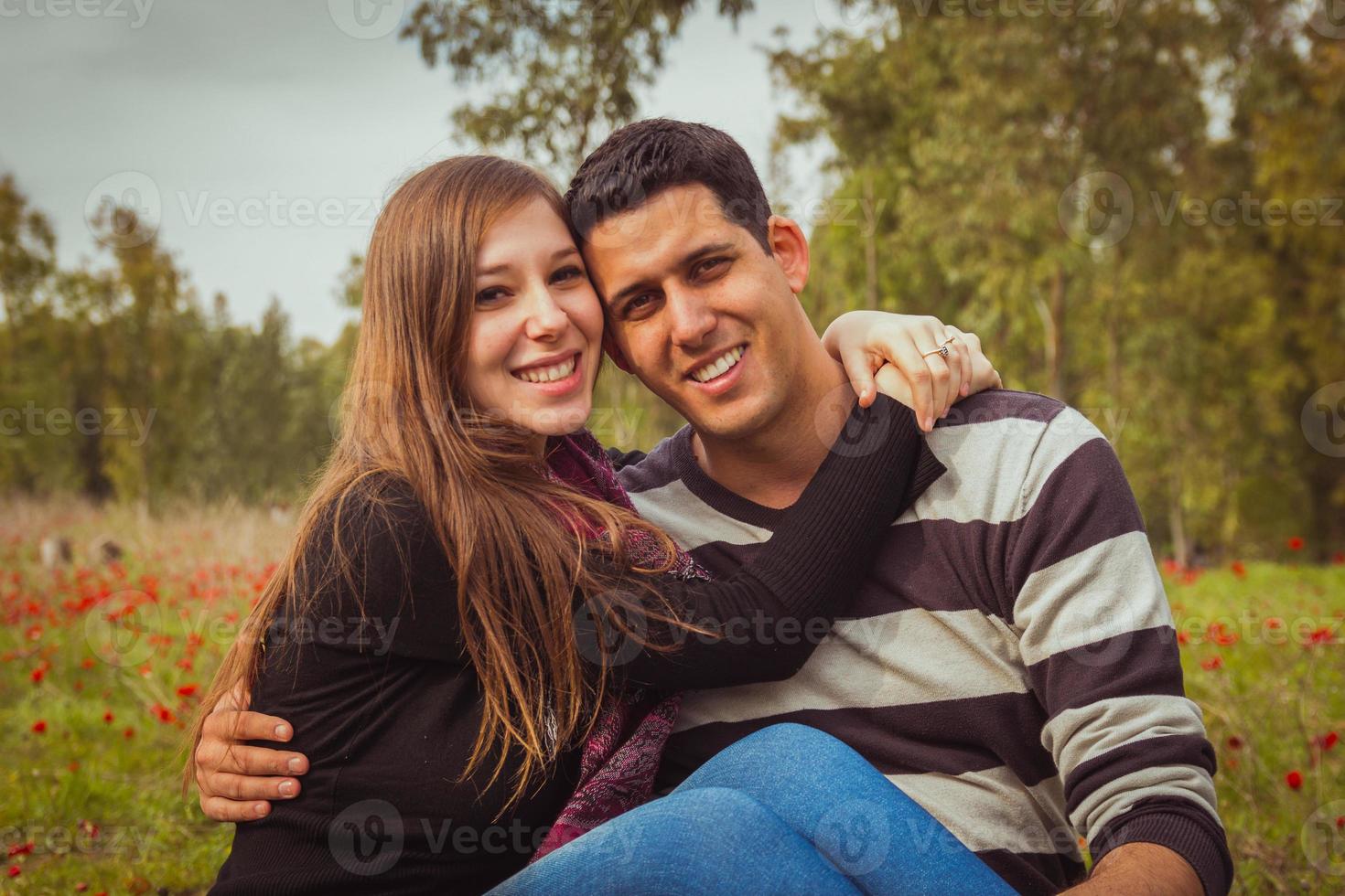 ungt par som sitter på gräset i ett fält av röda vallmo och ler mot kameran foto