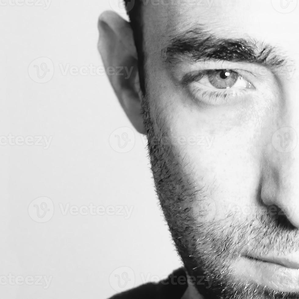 dramatisk närbild porträtt av en ung skäggig man halvt uttryckslösa ansikte på vit bakgrund tittar på kameran foto