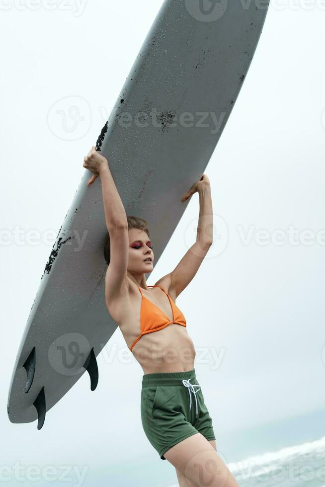 kvinna surfare bärande surfingbräda på huvud under sporter Träning. kvinna i bikini topp och shorts foto