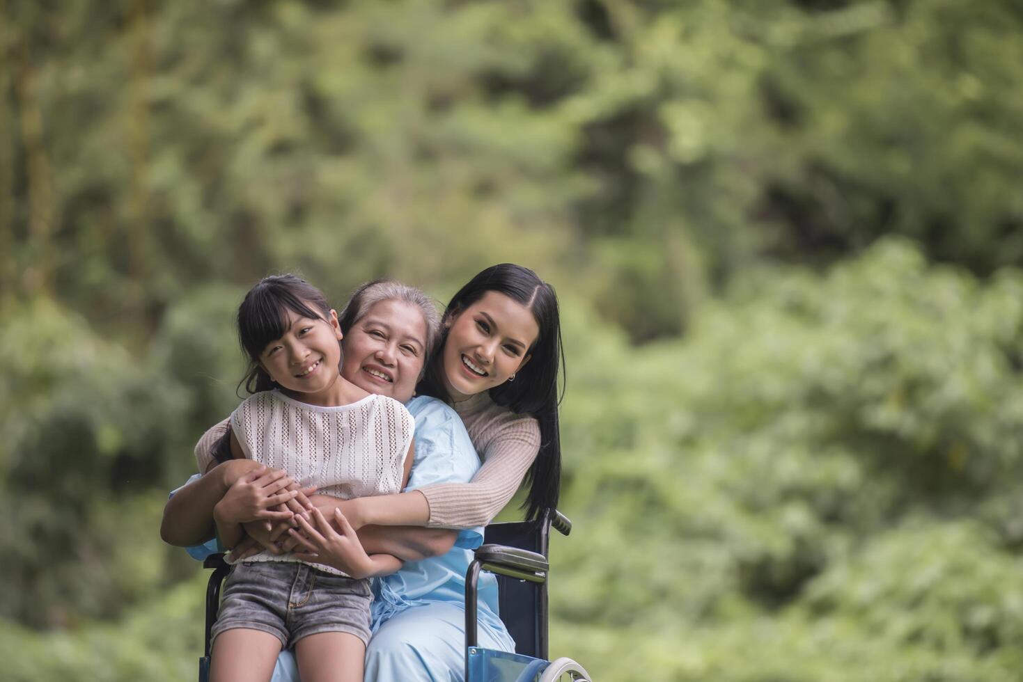 glad mormor i rullstol med sin dotter och barnbarn i en park, lyckligt liv lycklig tid. foto